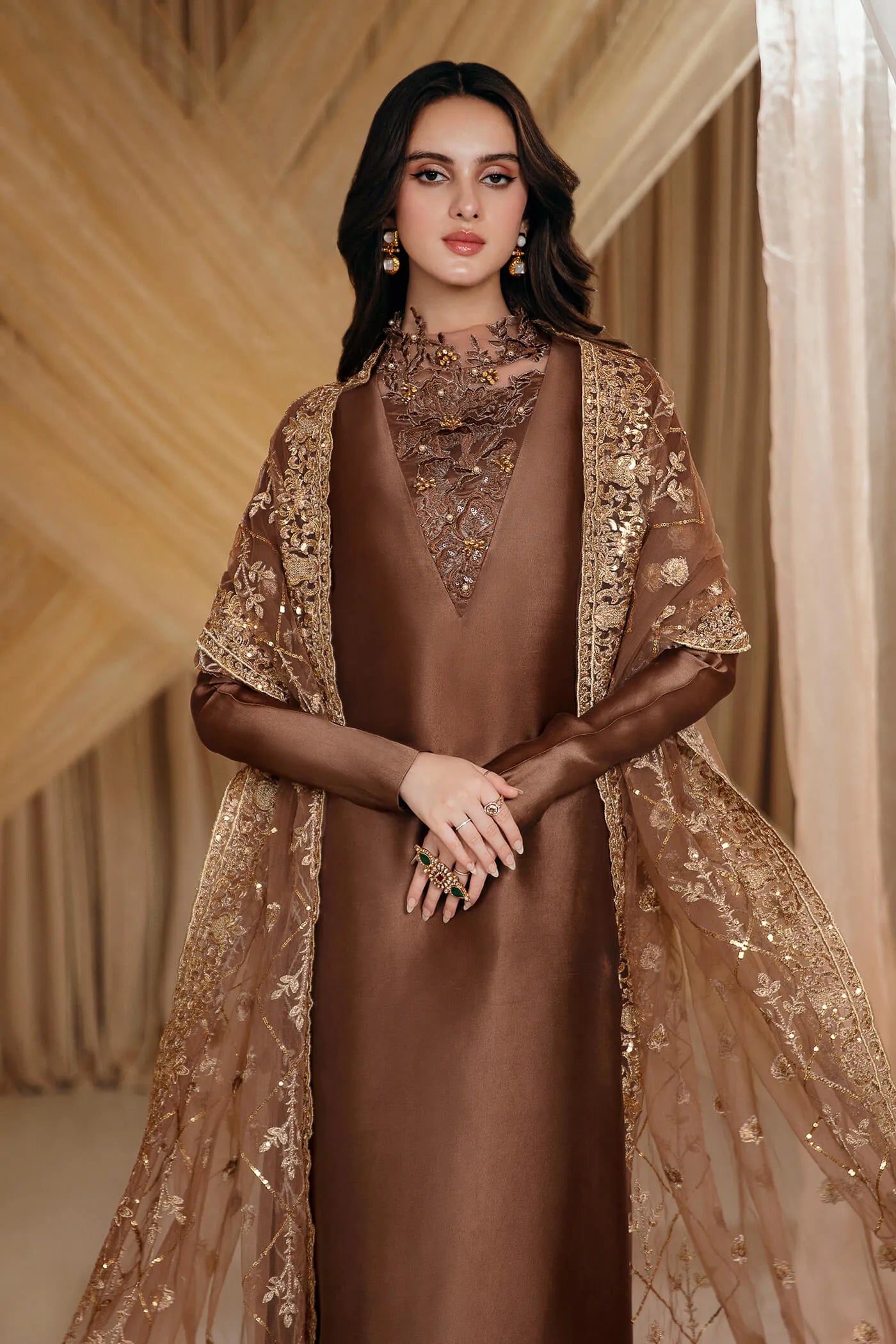 Model wearing Faiza Saqlain's Ethereal Goddess dress from the Musferah Saad Mystere Eid Collection '24. A luxurious brown Pakistani Eid dress adorned with intricate gold embroidery and an elegant dupatta, ideal for those seeking Pakistani designer clothes in the UK.