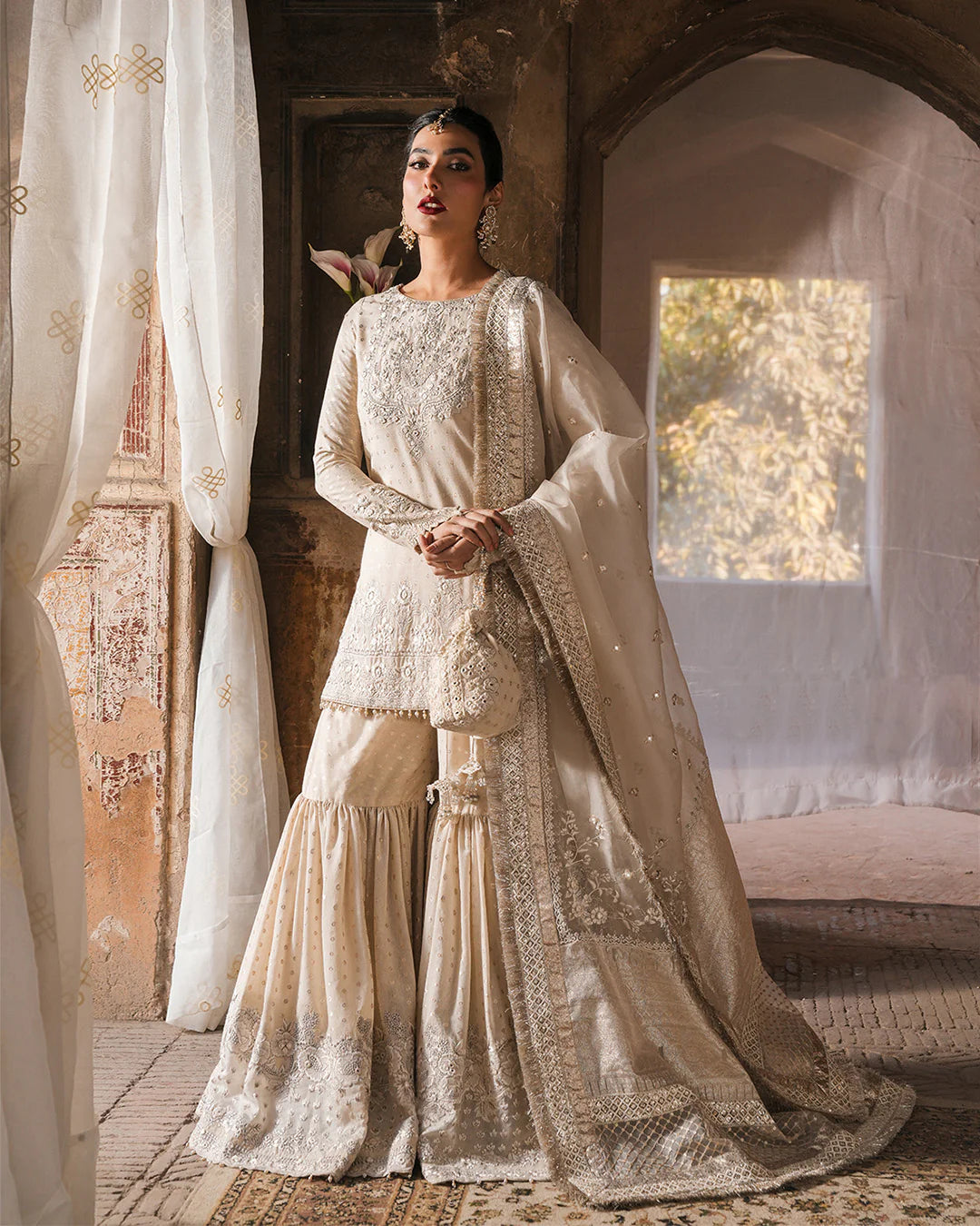 Model wearing ivory Faiza Saqlain Devina outfit with embellished gharara and dupatta, ideal for Pakistani luxury pret and festive wear in UK.