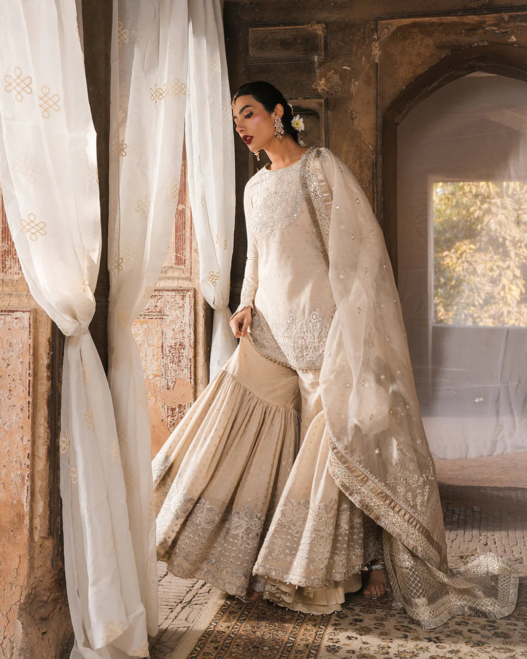 Model wearing ivory Faiza Saqlain Devina outfit with embellished gharara and dupatta, ideal for Pakistani luxury pret and festive wear in UK.