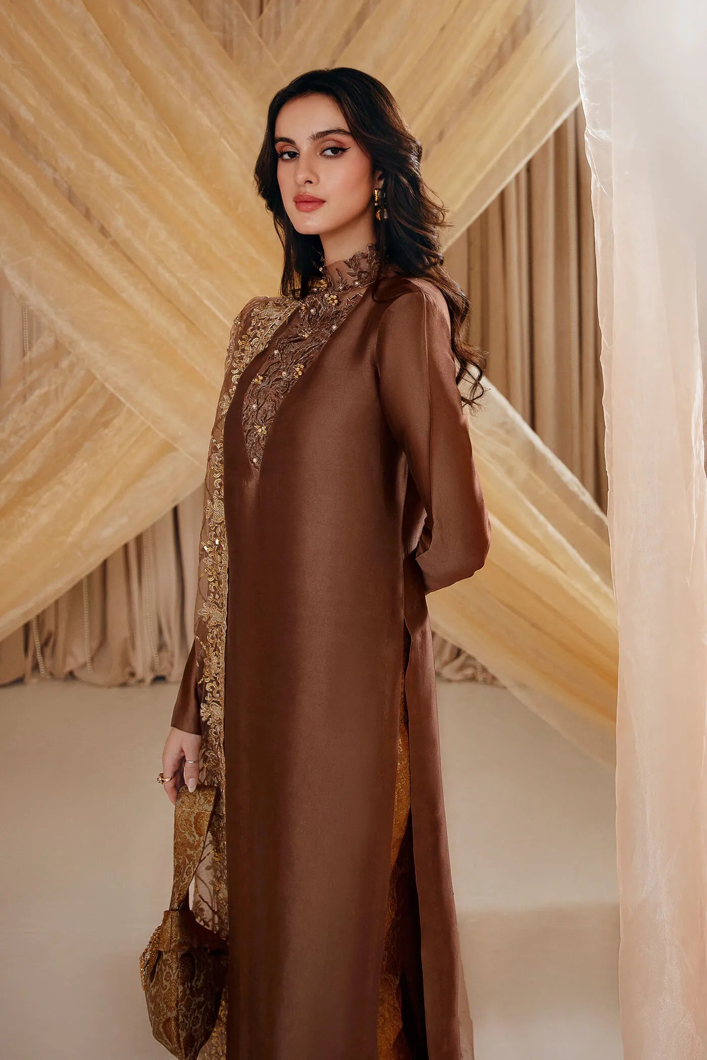 Model wearing Faiza Saqlain's Ethereal Goddess dress from the Musferah Saad Mystere Eid Collection '24. A luxurious brown Pakistani Eid dress adorned with intricate gold embroidery and an elegant dupatta, ideal for those seeking Pakistani designer clothes in the UK.