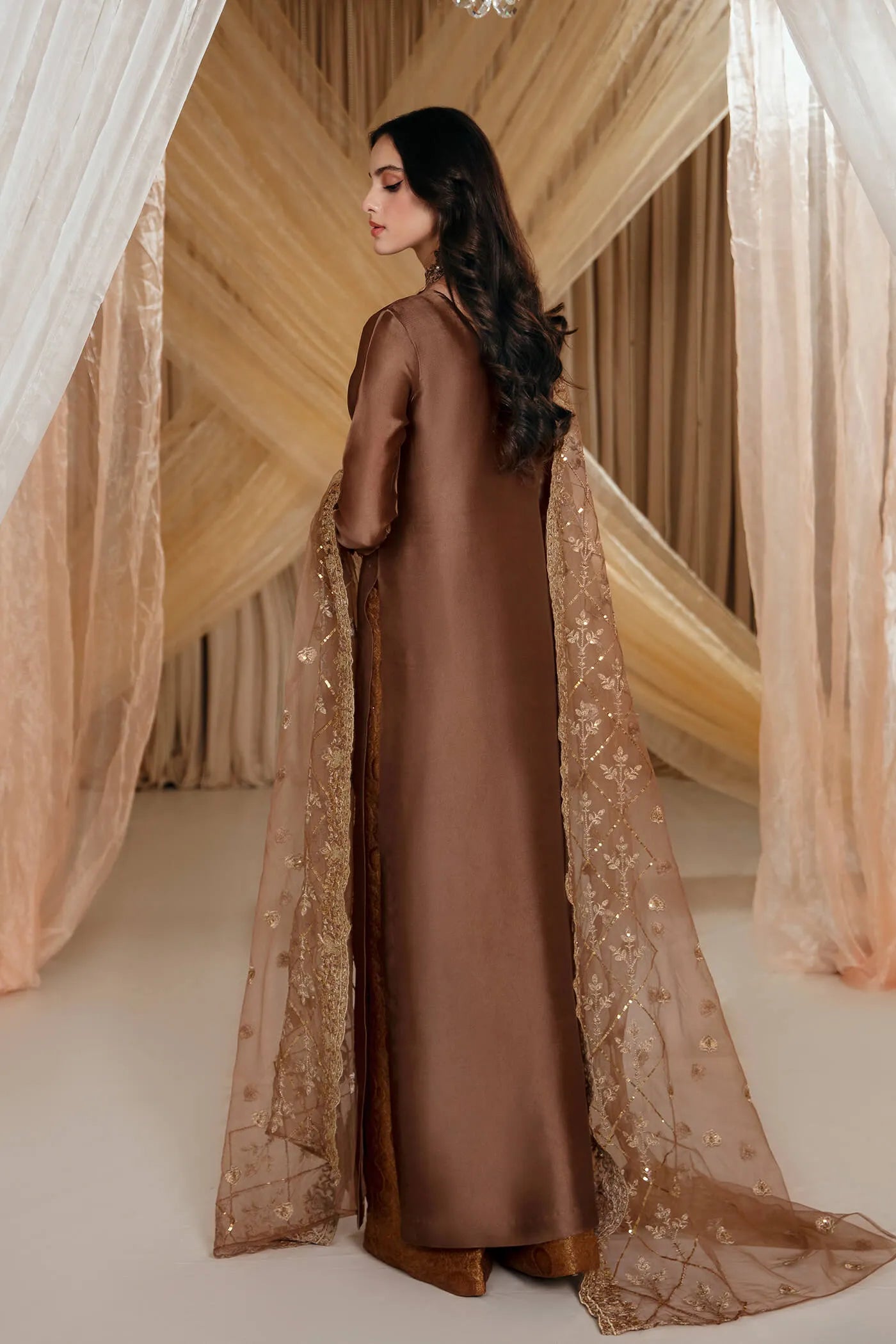 Model wearing Faiza Saqlain's Ethereal Goddess dress from the Musferah Saad Mystere Eid Collection '24. A luxurious brown Pakistani Eid dress adorned with intricate gold embroidery and an elegant dupatta, ideal for those seeking Pakistani designer clothes in the UK.