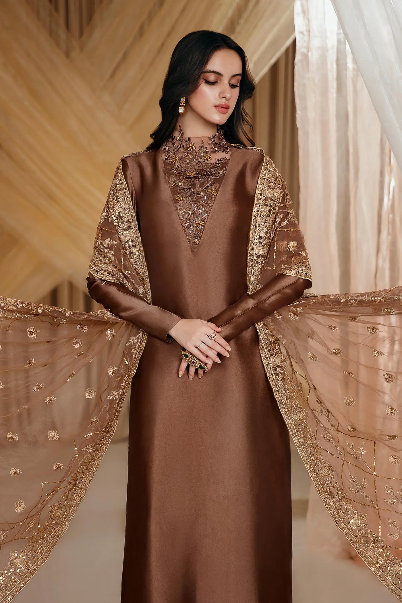 Model wearing Faiza Saqlain's Ethereal Goddess dress from the Musferah Saad Mystere Eid Collection '24. A luxurious brown Pakistani Eid dress adorned with intricate gold embroidery and an elegant dupatta, ideal for those seeking Pakistani designer clothes in the UK.
