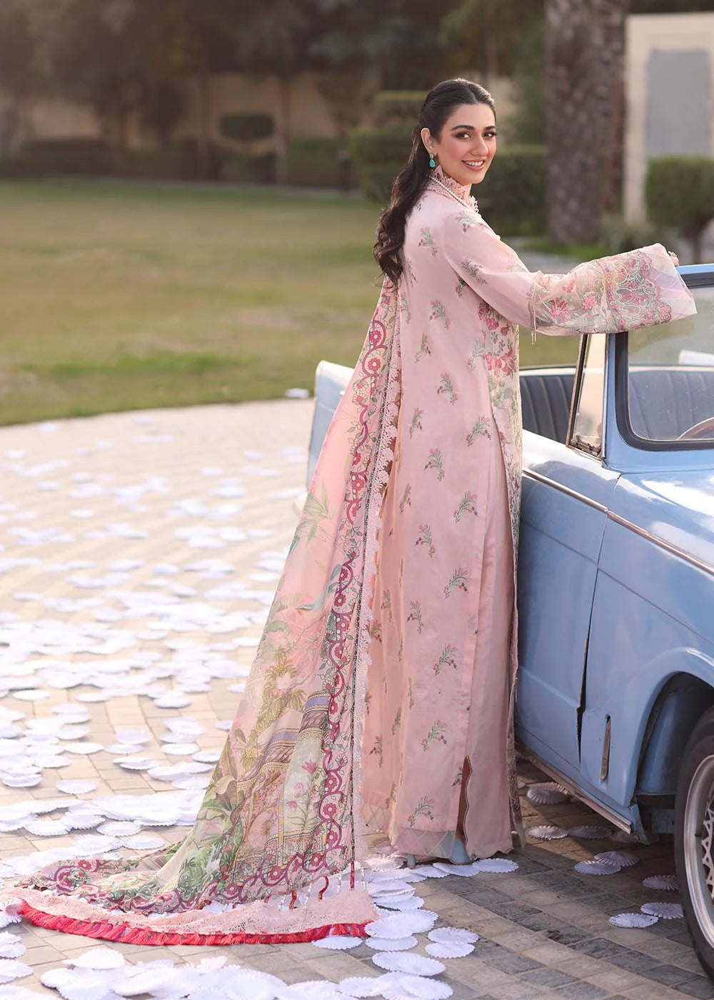 Model wearing pastel pink floral printed dress with lace neckline and embroidered dupatta from Musferah Saad Pretty Girls Luxury Lawn 2025 Bloome. Pakistani clothes online UK.