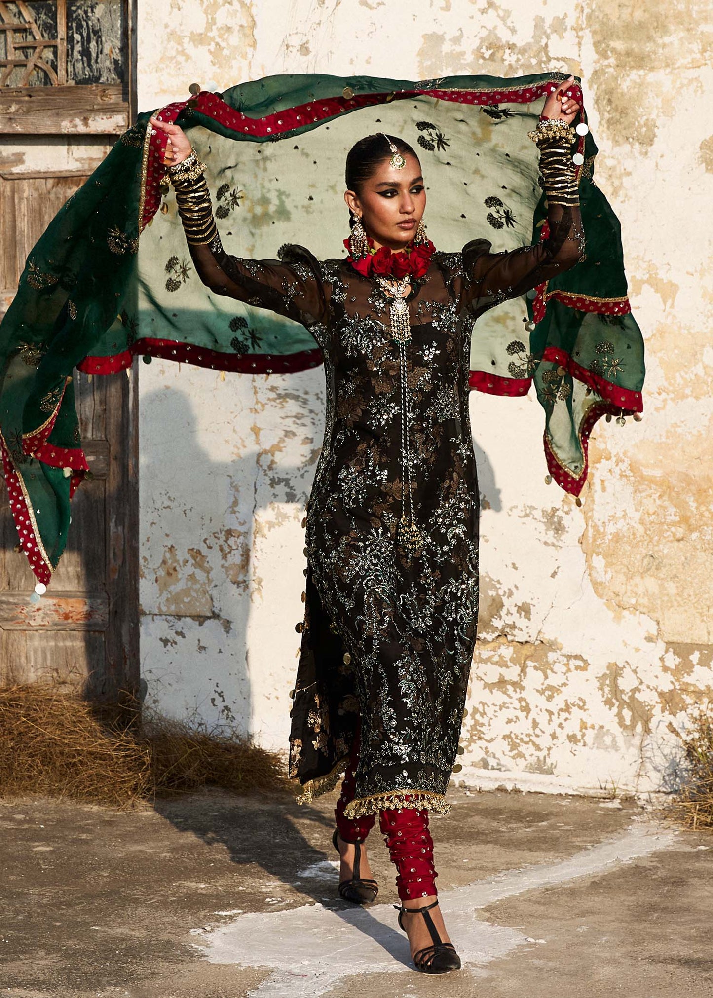 Model wearing Hussain Rehar Shama black embroidered festive dress with green and red accents. Shop Pakistani clothes online in the UK now.