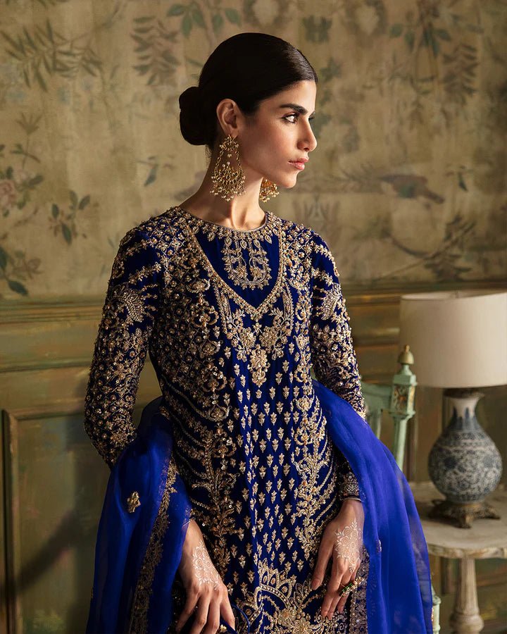 Model wearing a royal blue Seyhana dress with intricate gold embroidery from Faiza Saqlain's Luxe Formals Manaar Nov '23 collection. Pakistani clothes online in UK.