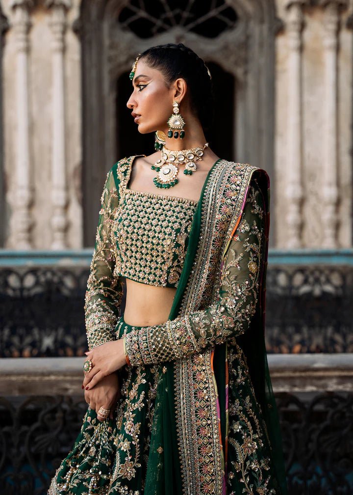 Model wearing a rich emerald green Sukhan lehenga from Kanwal Malik's Sajni II collection, embellished with intricate gold embroidery. Pakistani wedding clothes online in the UK.
