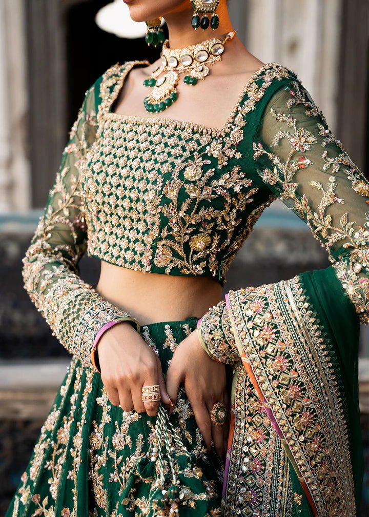 Model wearing a rich emerald green Sukhan lehenga from Kanwal Malik's Sajni II collection, embellished with intricate gold embroidery. Pakistani wedding clothes online in the UK.