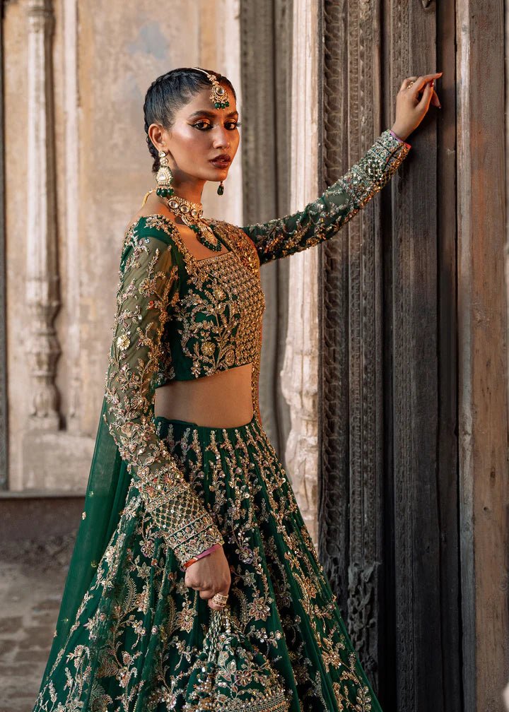 Model wearing a rich emerald green Sukhan lehenga from Kanwal Malik's Sajni II collection, embellished with intricate gold embroidery. Pakistani wedding clothes online in the UK.