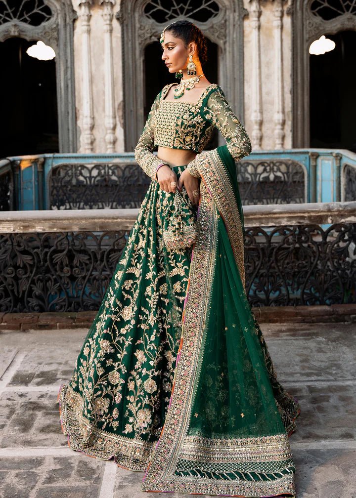 Model wearing a rich emerald green Sukhan lehenga from Kanwal Malik's Sajni II collection, embellished with intricate gold embroidery. Pakistani wedding clothes online in the UK.