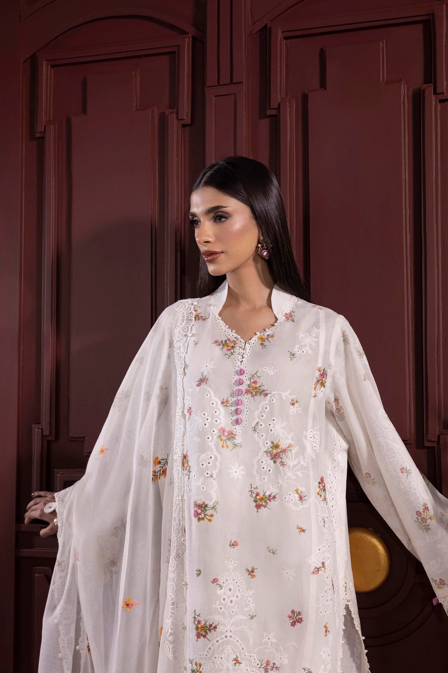 Model wearing white embroidered dress with multicolor floral accents and lace detailing from Sana Safinaz Muzlin Spring '25, Pakistani clothes online UK.