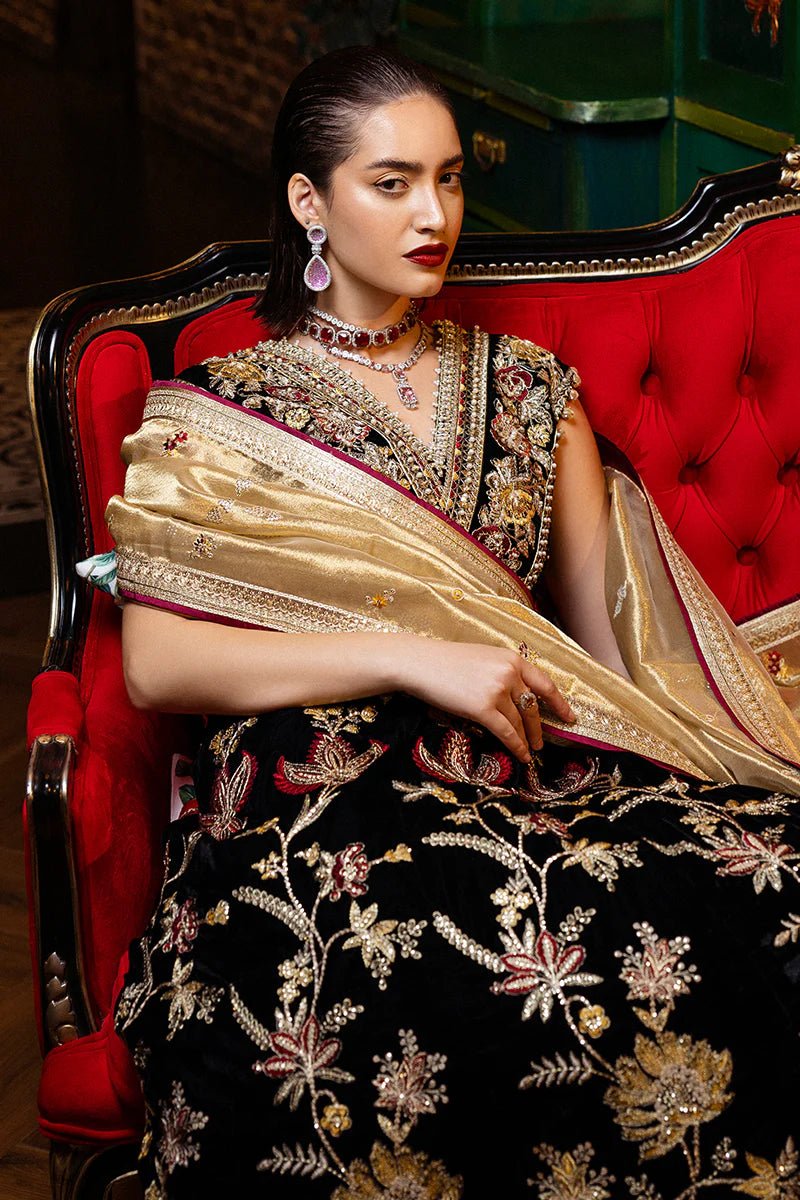 Model wearing Mushq DEJA VU - VELVET '24 Whispers of Yesterday, a black velvet gown with intricate gold and red floral embroidery, styled with a luxurious golden shawl. Ideal for winter weddings, available for Pakistani clothes online in the UK.