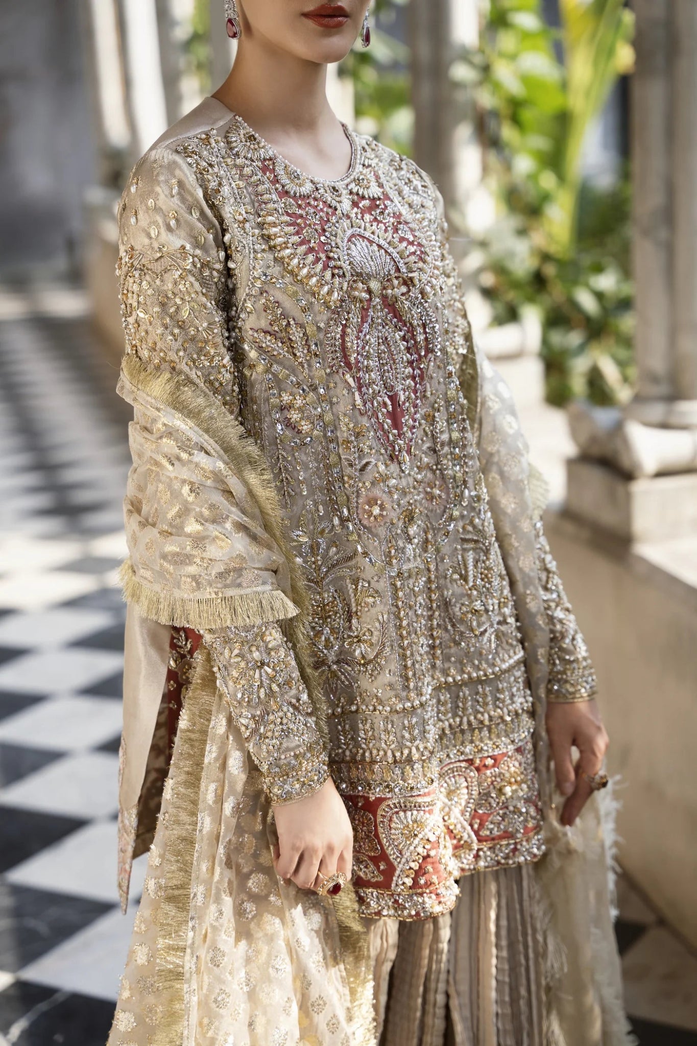 Model wearing a gold and red embellished GLEAM dress from Mysie by Tahira. Perfect for weddings, showcasing intricate embroidery. Shop Pakistani clothes online in the UK.