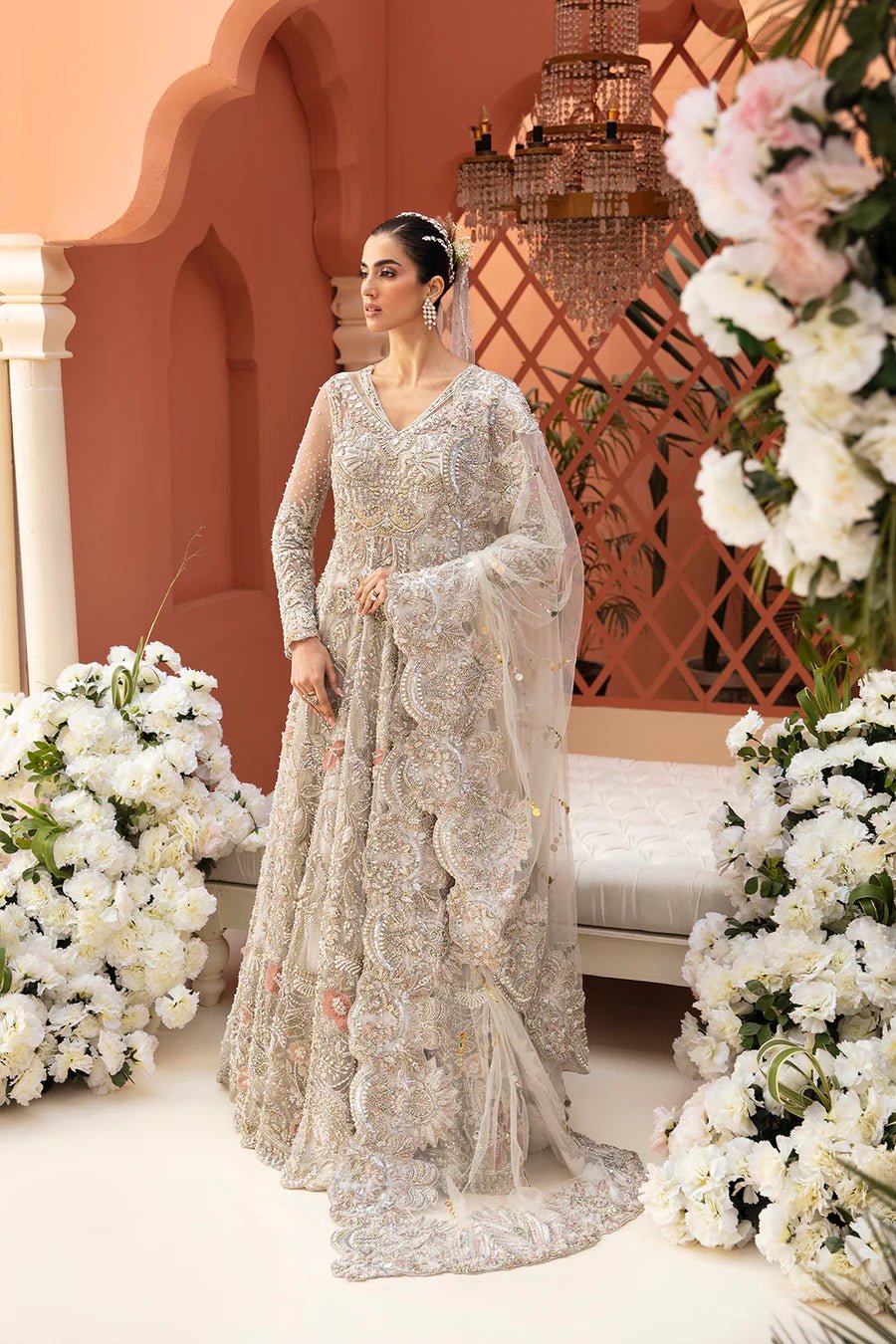 Model in a silver Mysie By Tahira Rylee bridal gown amidst flowers, showcasing exquisite Pakistani clothes UK.