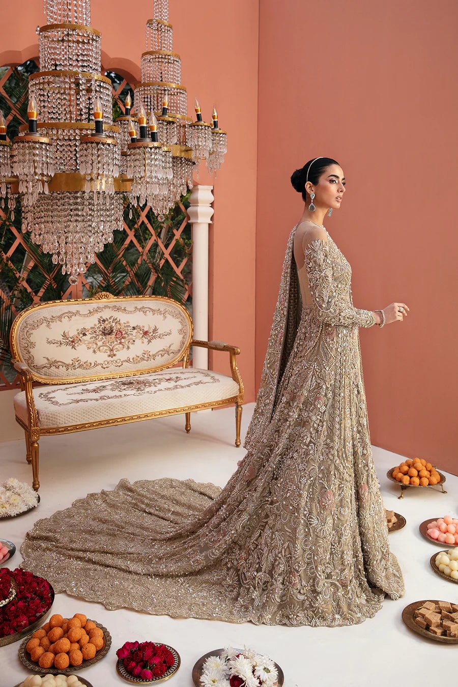 Model in Mysie By Tahira Savarna gold bridal gown, luxury Pakistani clothes UK, poised by chandeliers.