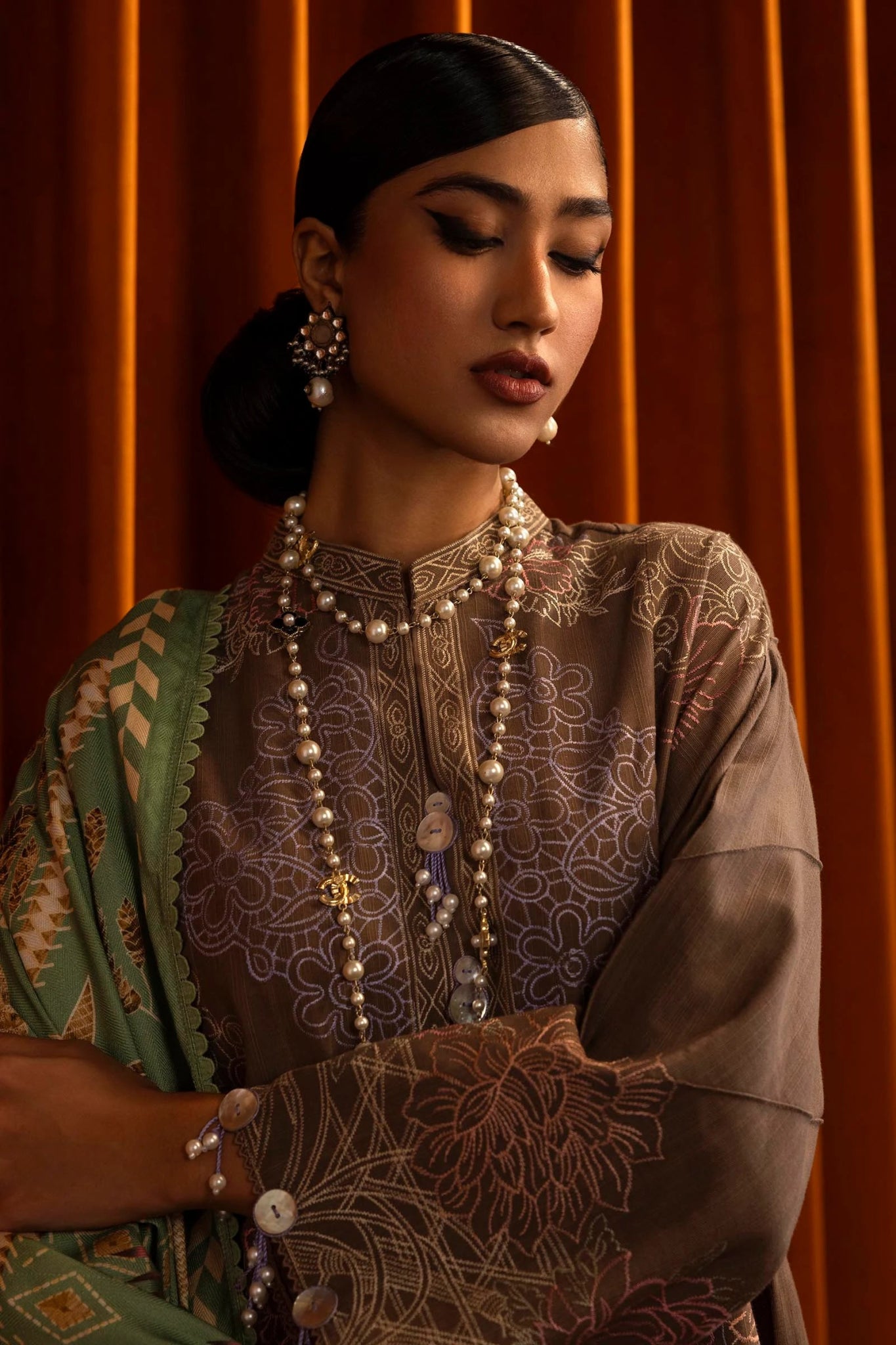A model is wearing a three - piece outfit from the Sana Safinaz Muzlin Winter '24 Collection. The ensemble features an embroidered front kali on slub fabric, paired with a dyed slub back and sleeves, all detailed with delicate embroidery. It includes a digitally printed shawl with intricate patterns, complemented by dyed cotton pants. The luxurious and sophisticated design, with its attention to detail, offers a chic choice for women seeking elegant Pakistani designer clothing. Available online