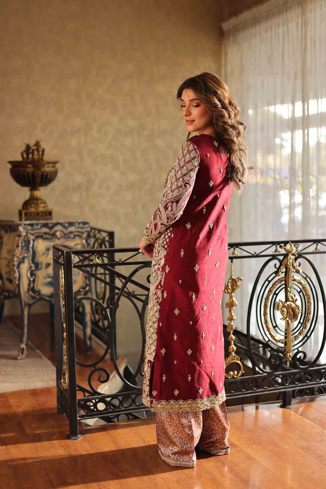 Model wearing deep maroon and gold hand-embellished long shirt with matching trousers from Mysie By Tahira Ruby, Pakistani Luxury pret UK.