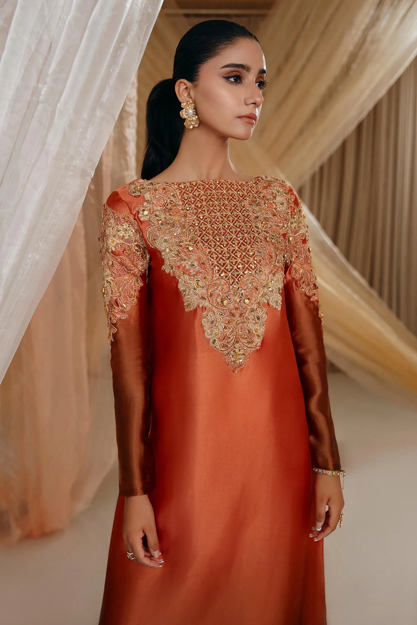 Model wearing Faiza Saqlain's Sunset Glow dress from the Musferah Saad Mystere Eid Collection '24. A stunning Pakistani Eid dress in burnt orange with intricate embroidery, ideal for Pakistani designer clothes lovers in the UK.