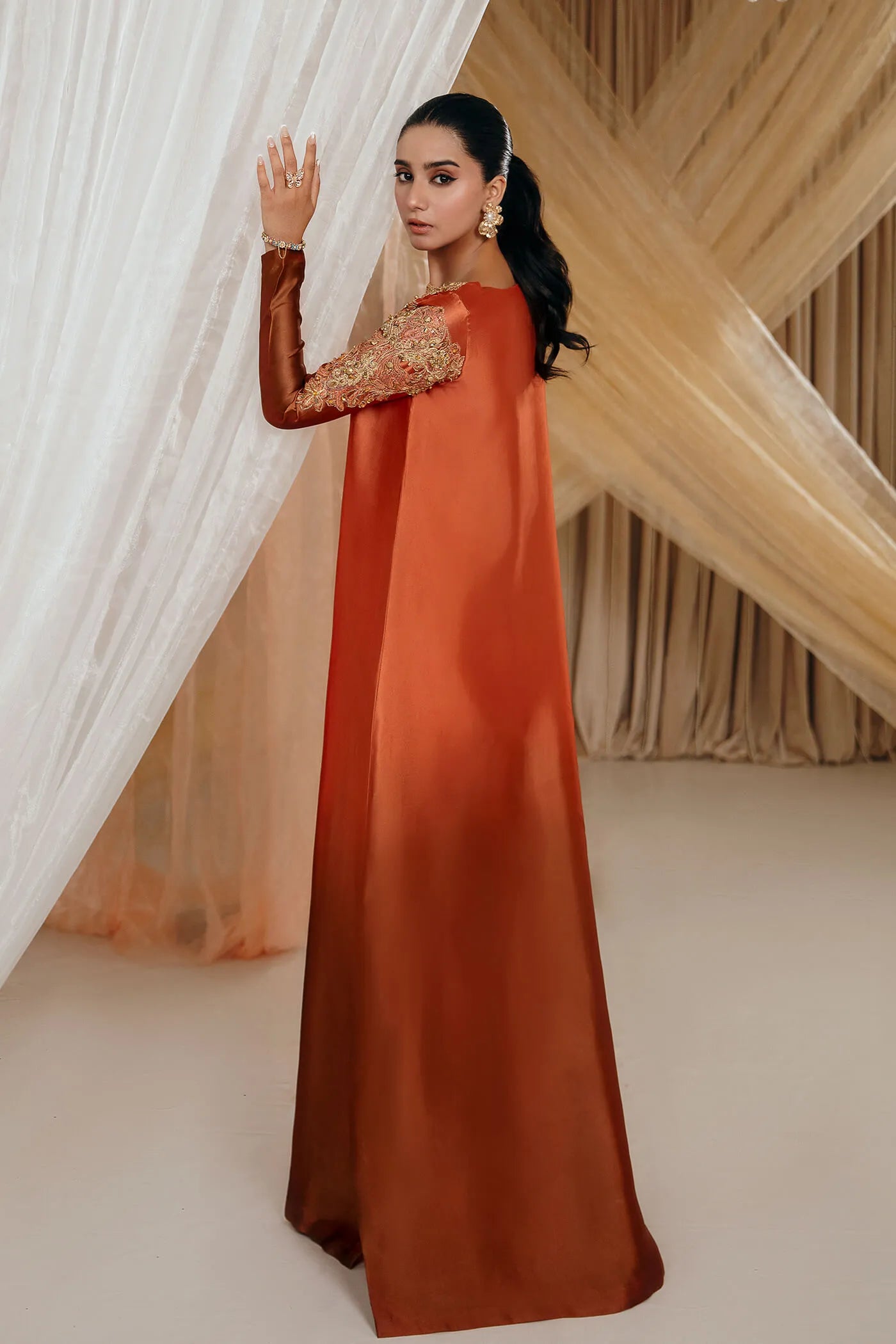 Model wearing Faiza Saqlain's Sunset Glow dress from the Musferah Saad Mystere Eid Collection '24. A stunning Pakistani Eid dress in burnt orange with intricate embroidery, ideal for Pakistani designer clothes lovers in the UK.