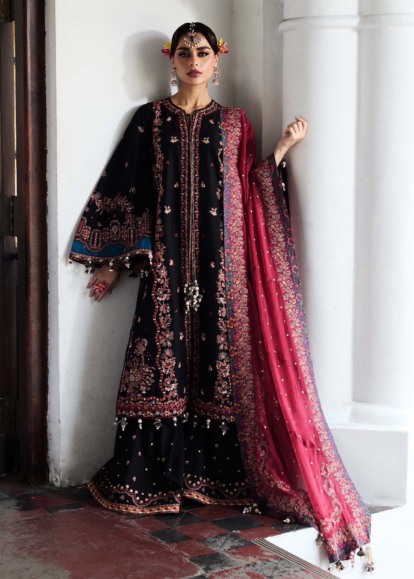 Model wearing Hussain Rehar Luxury Lawn '25 Bliz in black with intricate pink embroidery and a red dupatta. Shop Pakistani luxury pret online in the UK.