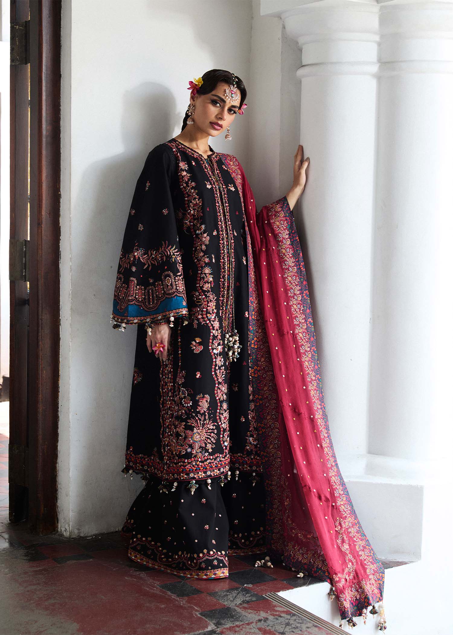 Model wearing Hussain Rehar Luxury Lawn '25 Bliz in black with intricate pink embroidery and a red dupatta. Shop Pakistani luxury pret online in the UK.