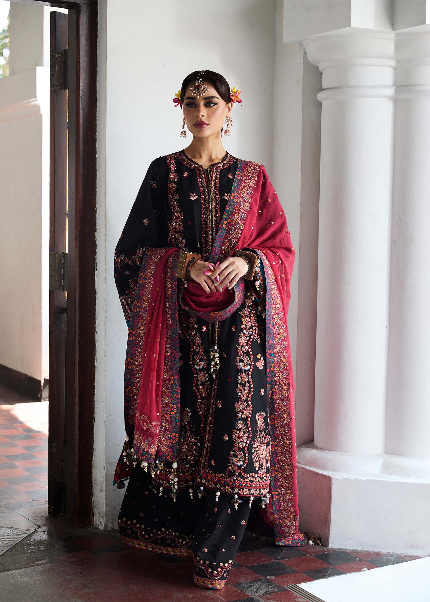 Model wearing Hussain Rehar Luxury Lawn '25 Bliz in black with intricate pink embroidery and a red dupatta. Shop Pakistani luxury pret online in the UK.