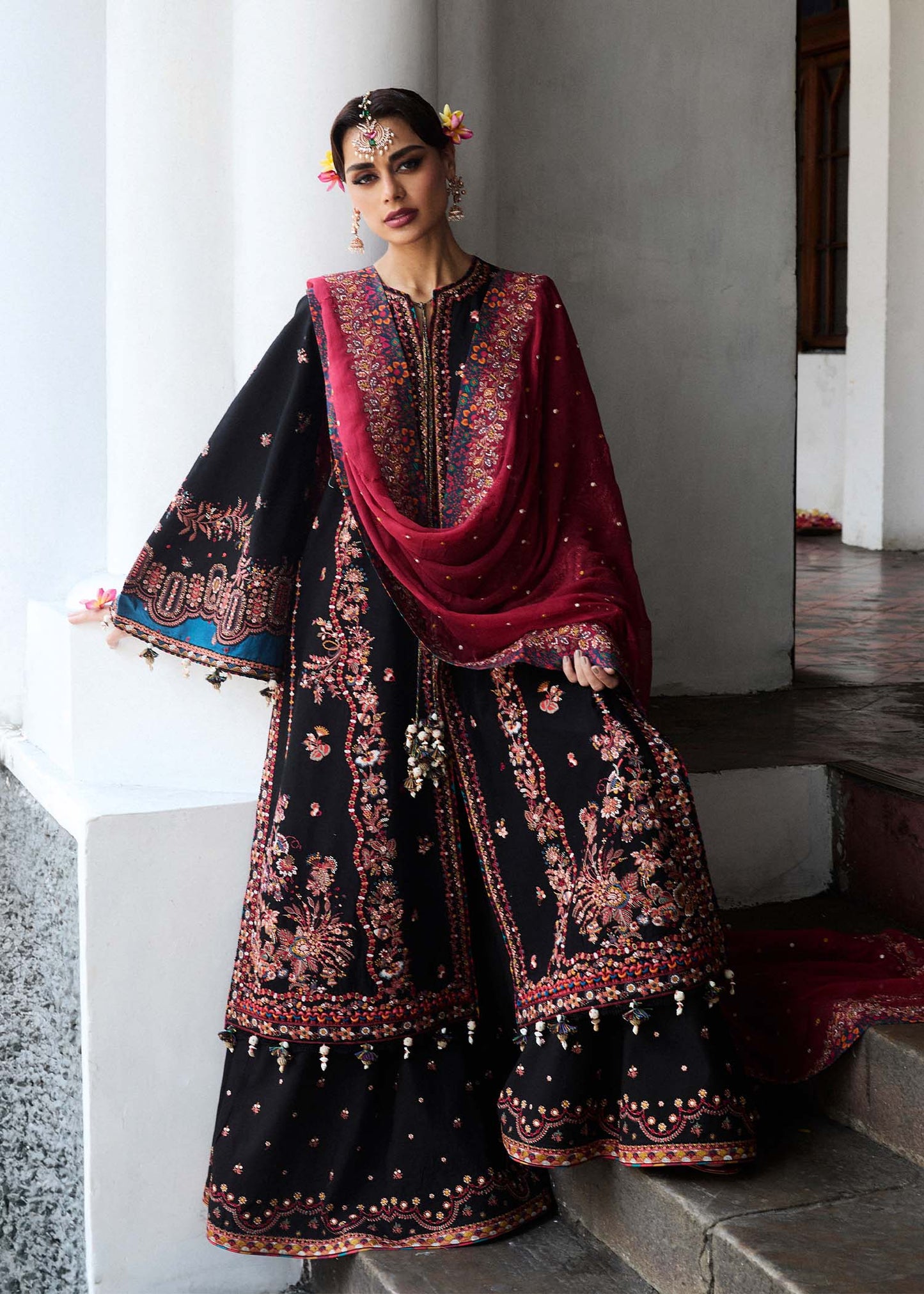 Model wearing Hussain Rehar Luxury Lawn '25 Bliz in black with intricate pink embroidery and a red dupatta. Shop Pakistani luxury pret online in the UK.