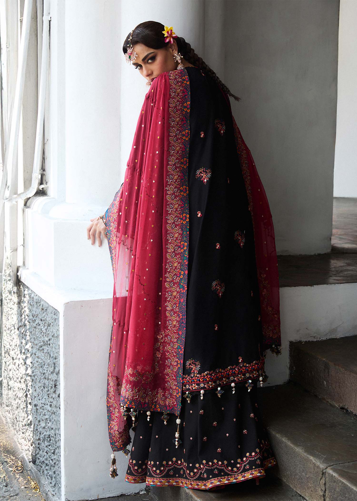 Model wearing Hussain Rehar Luxury Lawn '25 Bliz in black with intricate pink embroidery and a red dupatta. Shop Pakistani luxury pret online in the UK.