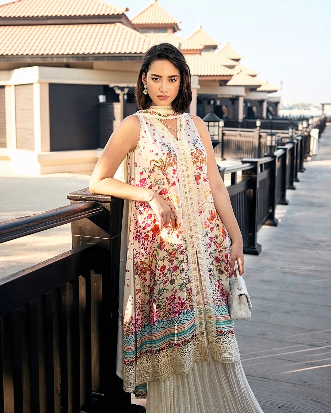 Model wearing Faiza Saqlain’s Beldene from the Carmela collection, featuring a cream embroidered silk shirt with floral patterns, paired with a crushed silk sharara and printed chiffon dupatta. Perfect for Pakistani clothes UK.