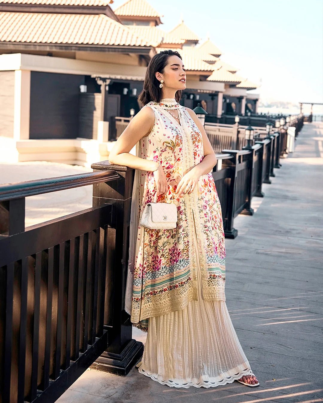 Model wearing Faiza Saqlain’s Beldene from the Carmela collection, featuring a cream embroidered silk shirt with floral patterns, paired with a crushed silk sharara and printed chiffon dupatta. Perfect for Pakistani clothes UK.