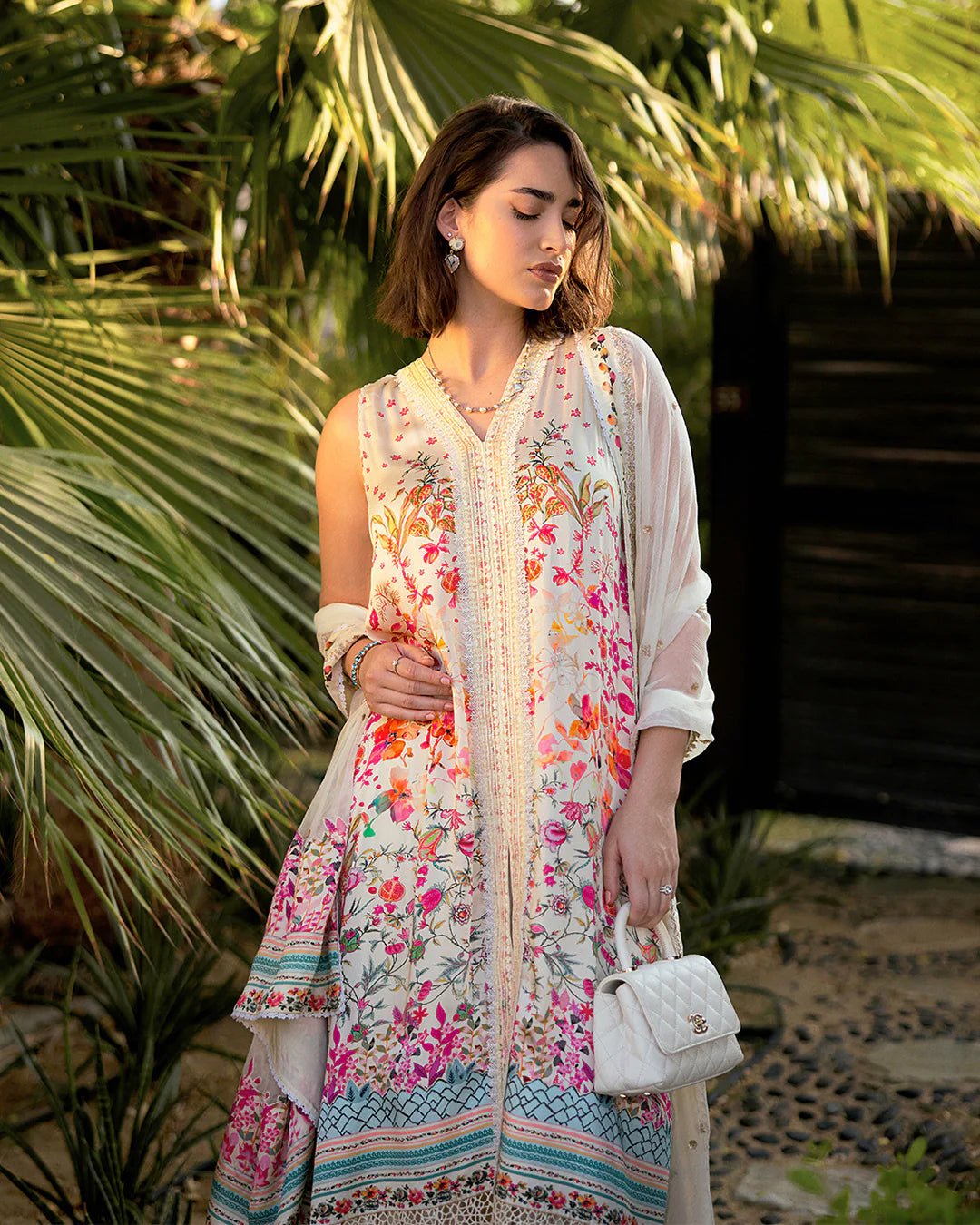 Model wearing Faiza Saqlain’s Beldene from the Carmela collection, featuring a cream embroidered silk shirt with floral patterns, paired with a crushed silk sharara and printed chiffon dupatta. Perfect for Pakistani clothes UK.