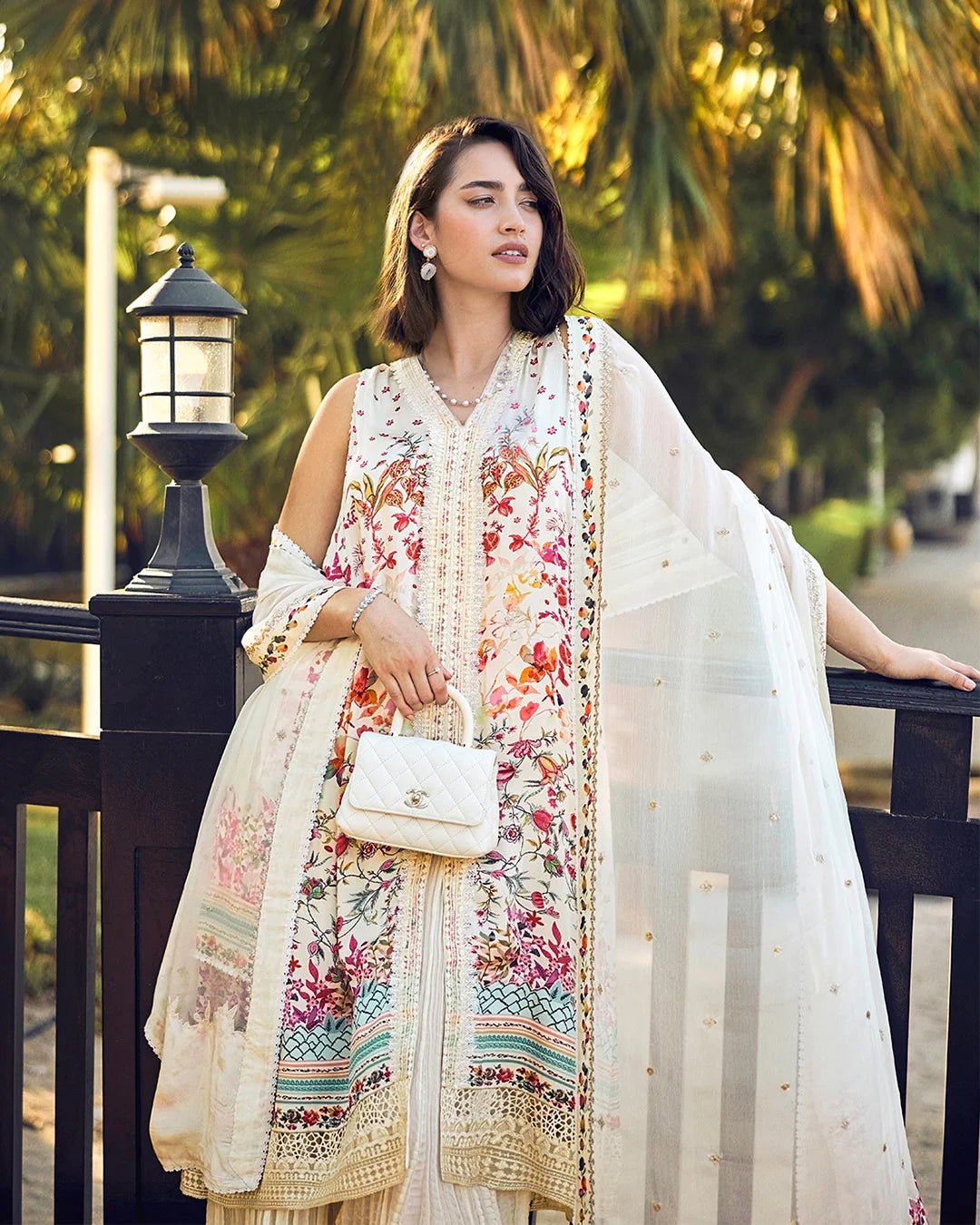 Model wearing Faiza Saqlain’s Beldene from the Carmela collection, featuring a cream embroidered silk shirt with floral patterns, paired with a crushed silk sharara and printed chiffon dupatta. Perfect for Pakistani clothes UK.