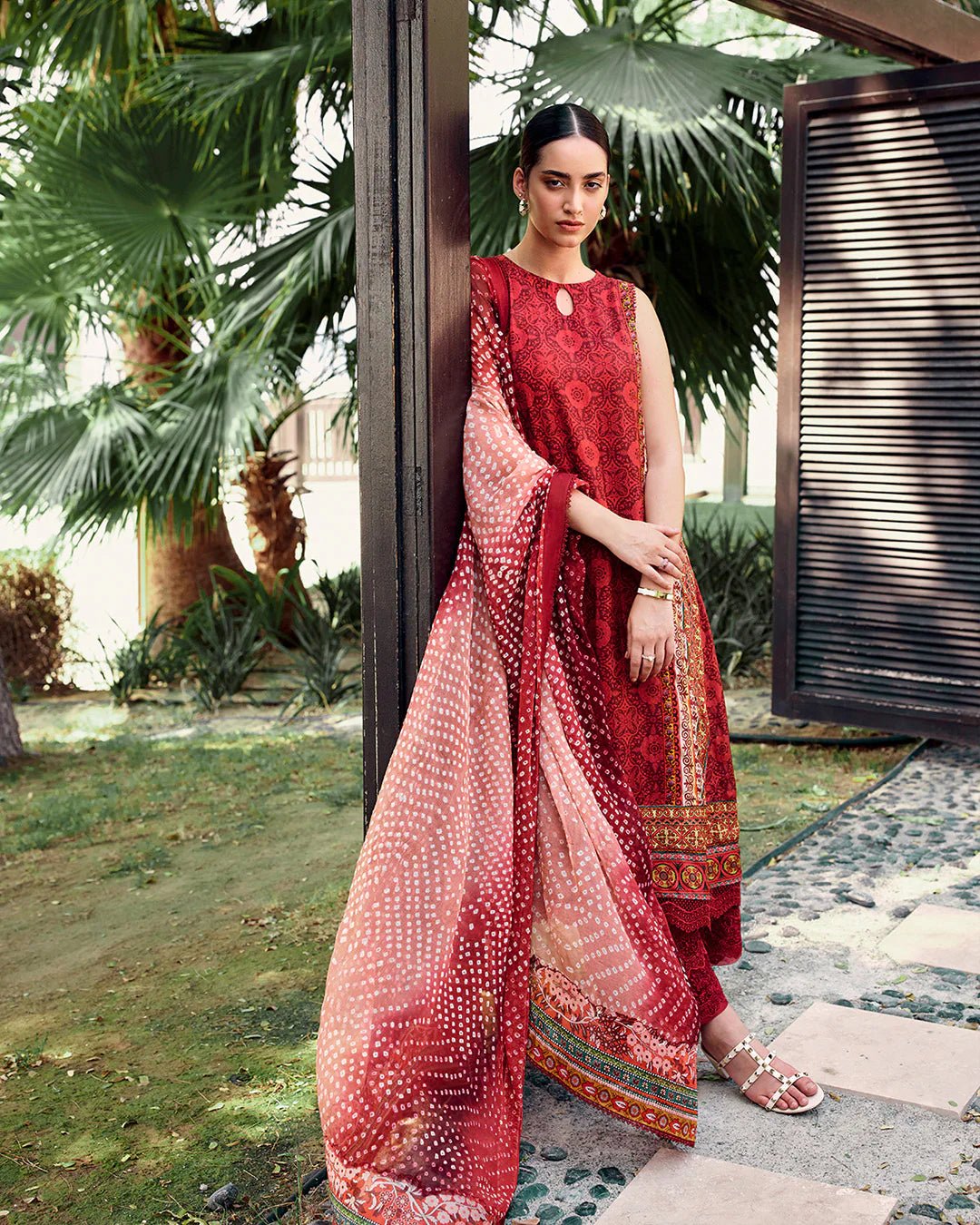 Model wearing Faiza Saqlain Carmela Gloriana dress in rich red with intricate patterns and a vibrant printed dupatta. Shop Pakistani bridal dresses online in the UK now.