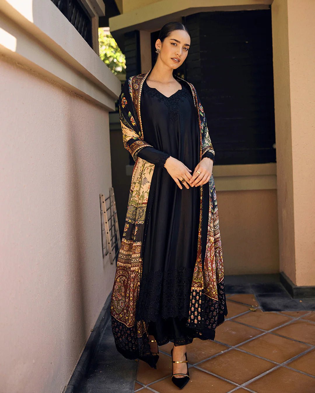 Model wearing Faiza Saqlain Carmela Shelina dress in black with intricate detailing and a vibrant printed shawl. Shop Pakistani bridal dresses online in the UK now.