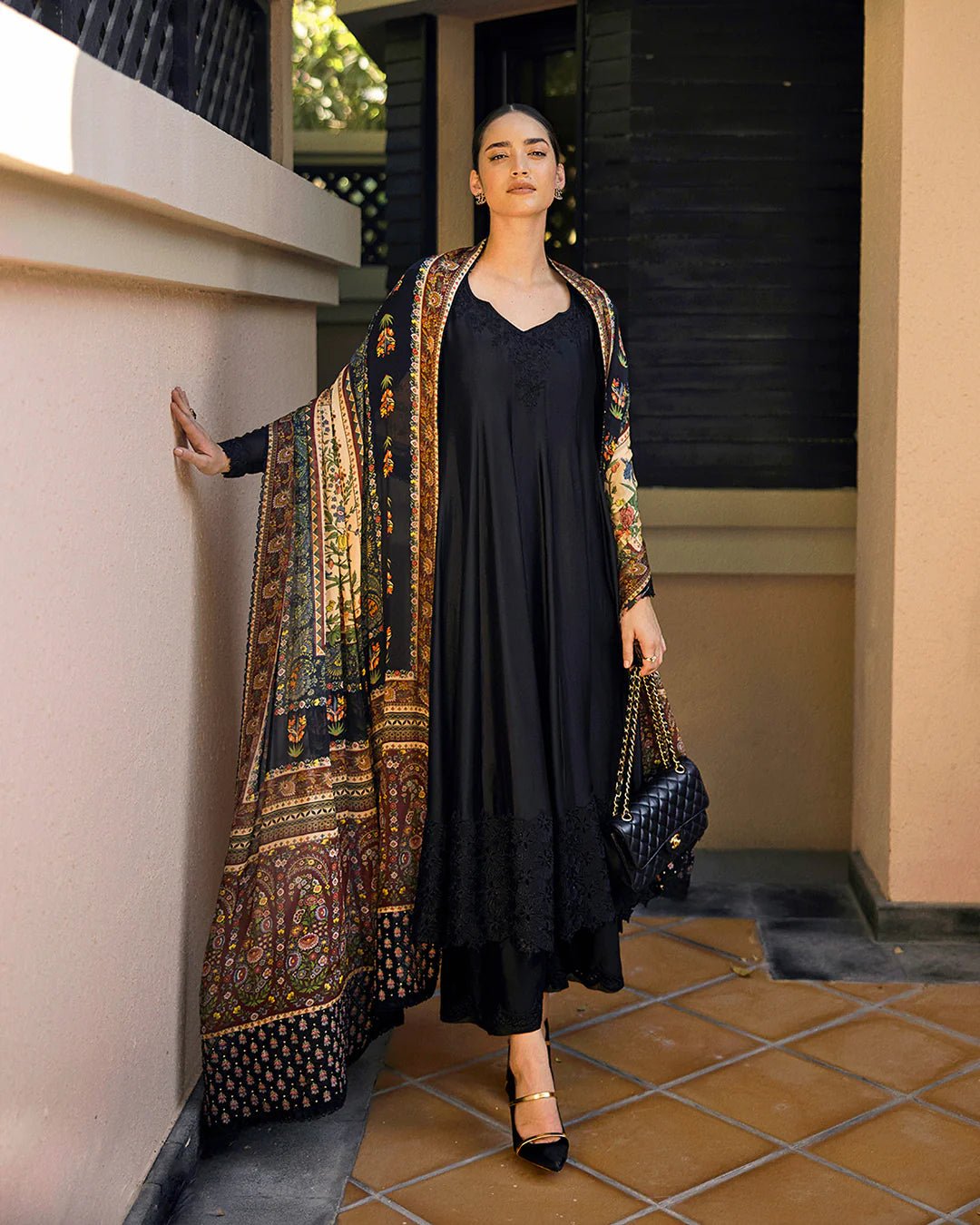 Model wearing Faiza Saqlain Carmela Shelina dress in black with intricate detailing and a vibrant printed shawl. Shop Pakistani bridal dresses online in the UK now.