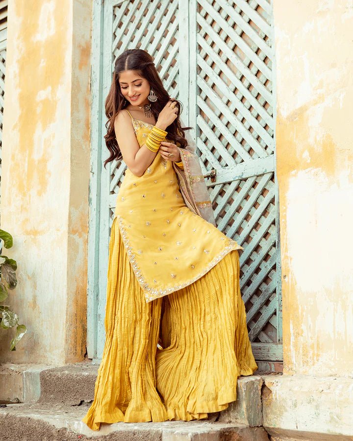 Model wearing Faiza Saqlain Fara dress in yellow mehndi dress from the Dhoop Kinaray Formals collection, ideal for weddings, available for Pakistani clothes online in the UK.