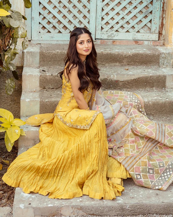 Model wearing Faiza Saqlain Fara dress in yellow mehndi dress from the Dhoop Kinaray Formals collection, ideal for weddings, available for Pakistani clothes online in the UK.