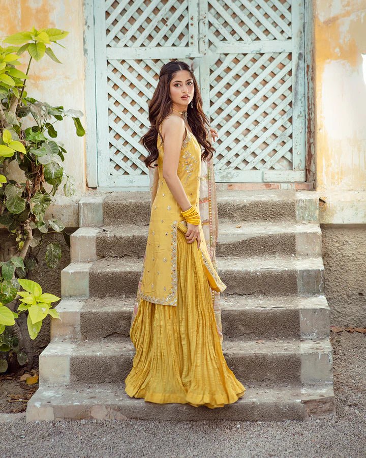 Model wearing Faiza Saqlain Fara dress in yellow mehndi dress from the Dhoop Kinaray Formals collection, ideal for weddings, available for Pakistani clothes online in the UK.