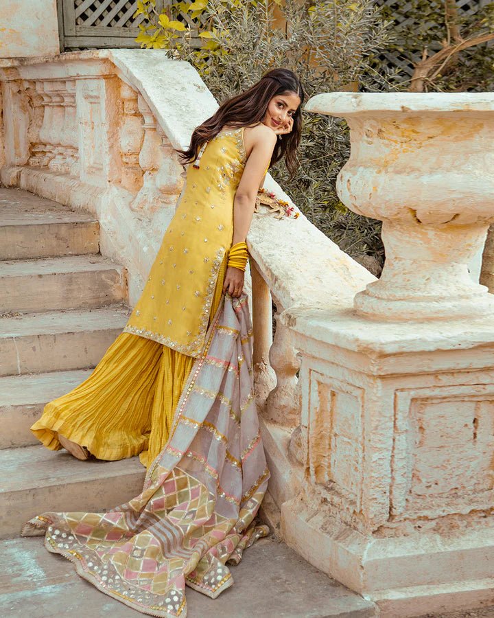 Model wearing Faiza Saqlain Fara dress in yellow mehndi dress from the Dhoop Kinaray Formals collection, ideal for weddings, available for Pakistani clothes online in the UK.