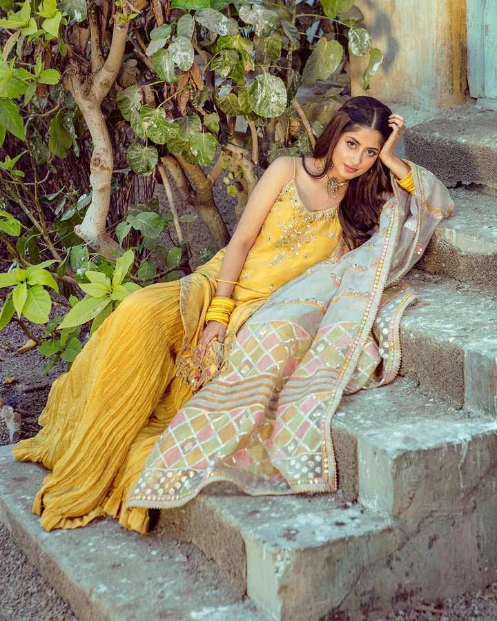 Model wearing Faiza Saqlain Fara dress in yellow mehndi dress from the Dhoop Kinaray Formals collection, ideal for weddings, available for Pakistani clothes online in the UK.