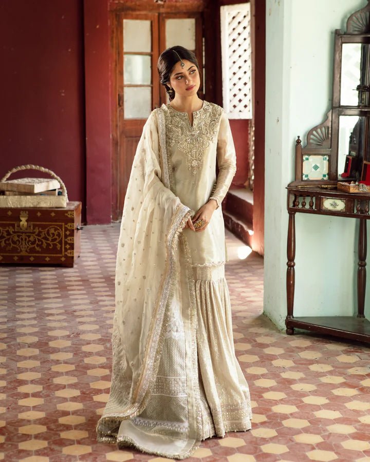 Model wearing Faiza Saqlain MINHA dress in ivory from the Dhoop Kinaray Formals collection, perfect for Pakistani weddings and formals, available online in the UK.