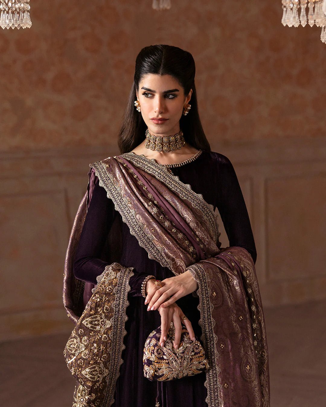 Model wearing Faiza Saqlain Ismene Velvet Erna dress in deep plum with intricate gold embroidery and an embellished dupatta. Shop Pakistani bridal dresses online in the UK now.