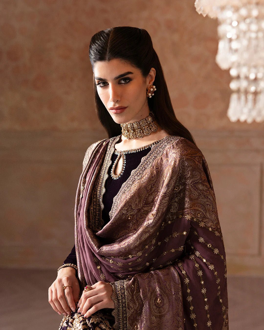 Model wearing Faiza Saqlain Ismene Velvet Erna dress in deep plum with intricate gold embroidery and an embellished dupatta. Shop Pakistani bridal dresses online in the UK now.