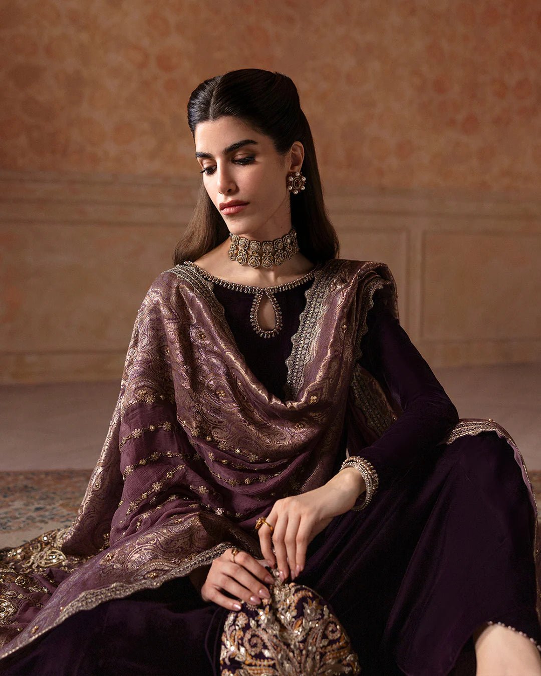 Model wearing Faiza Saqlain Ismene Velvet Erna dress in deep plum with intricate gold embroidery and an embellished dupatta. Shop Pakistani bridal dresses online in the UK now.