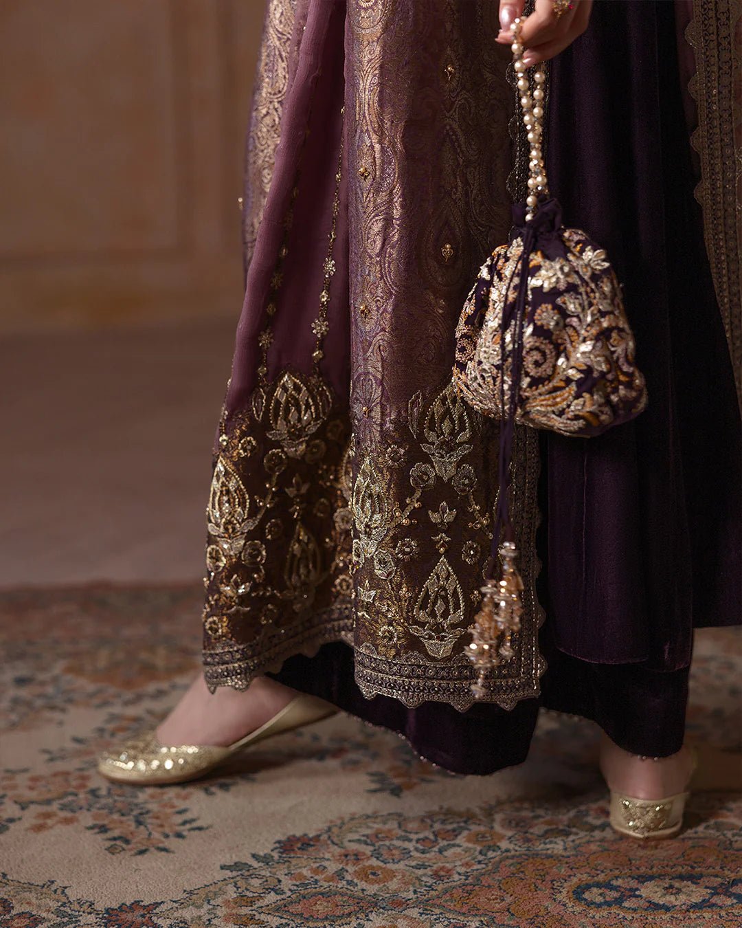 Model wearing Faiza Saqlain Ismene Velvet Erna dress in deep plum with intricate gold embroidery and an embellished dupatta. Shop Pakistani bridal dresses online in the UK now.