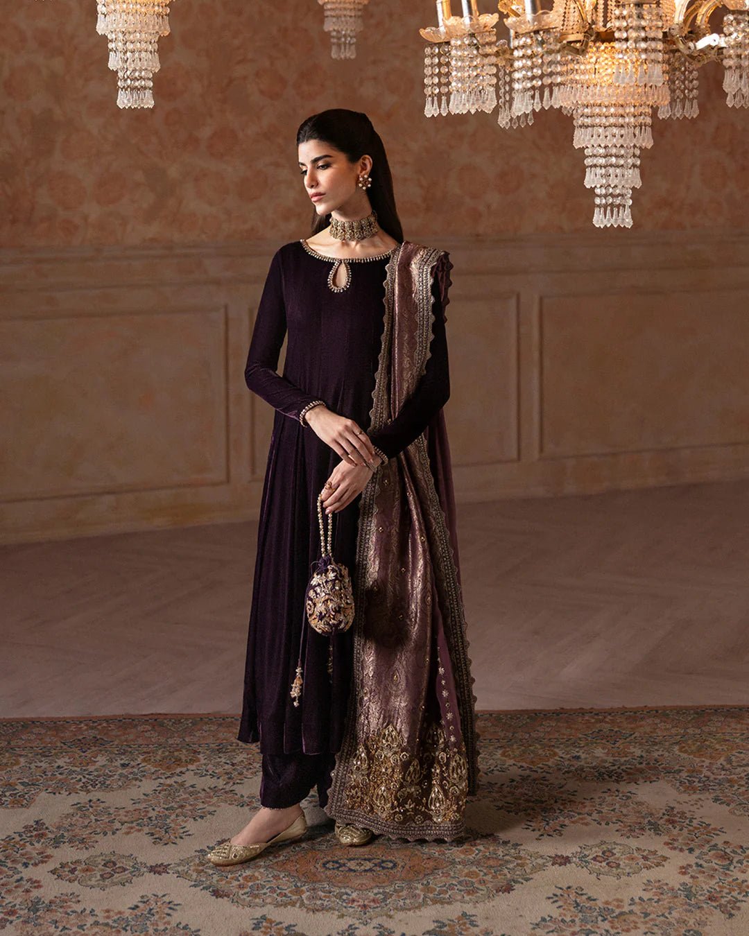 Model wearing Faiza Saqlain Ismene Velvet Erna dress in deep plum with intricate gold embroidery and an embellished dupatta. Shop Pakistani bridal dresses online in the UK now.