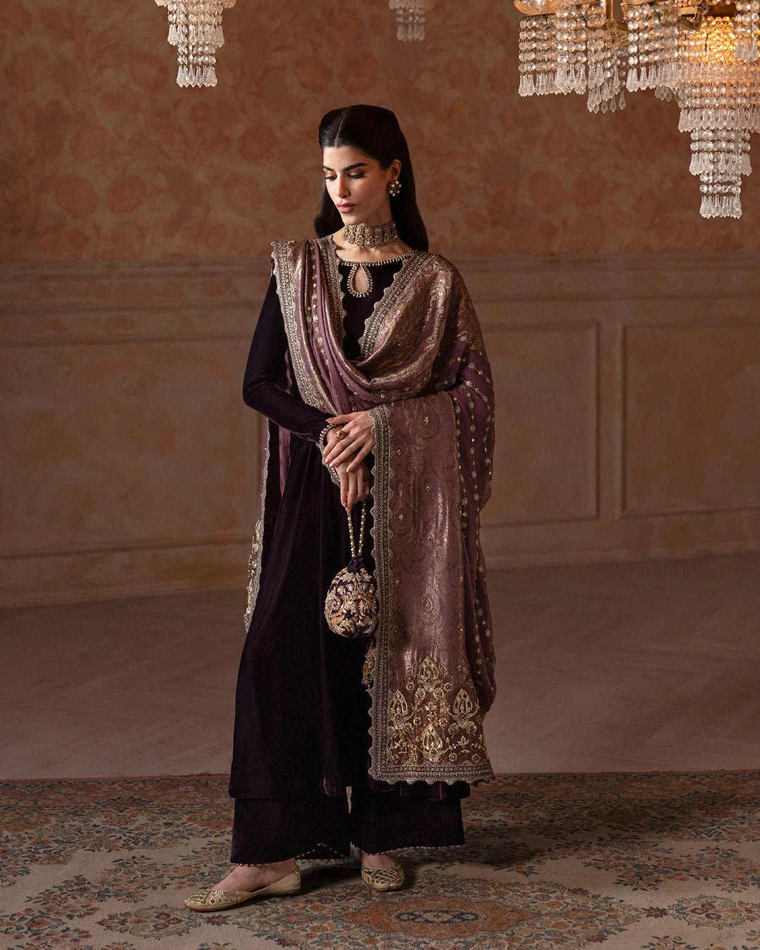 Model wearing Faiza Saqlain Ismene Velvet Erna dress in deep plum with intricate gold embroidery and an embellished dupatta. Shop Pakistani bridal dresses online in the UK now.