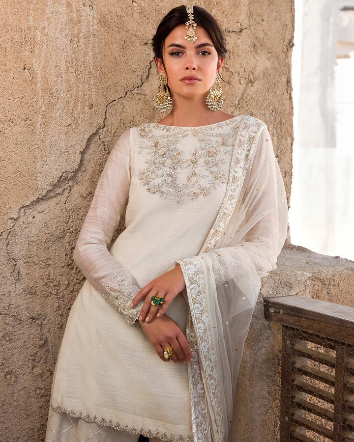 Model wearing an elegant ivory Raabi dress adorned with delicate embroidery from Faiza Saqlain's Luxe Formals Laira collection. Pakistani clothes online in UK.