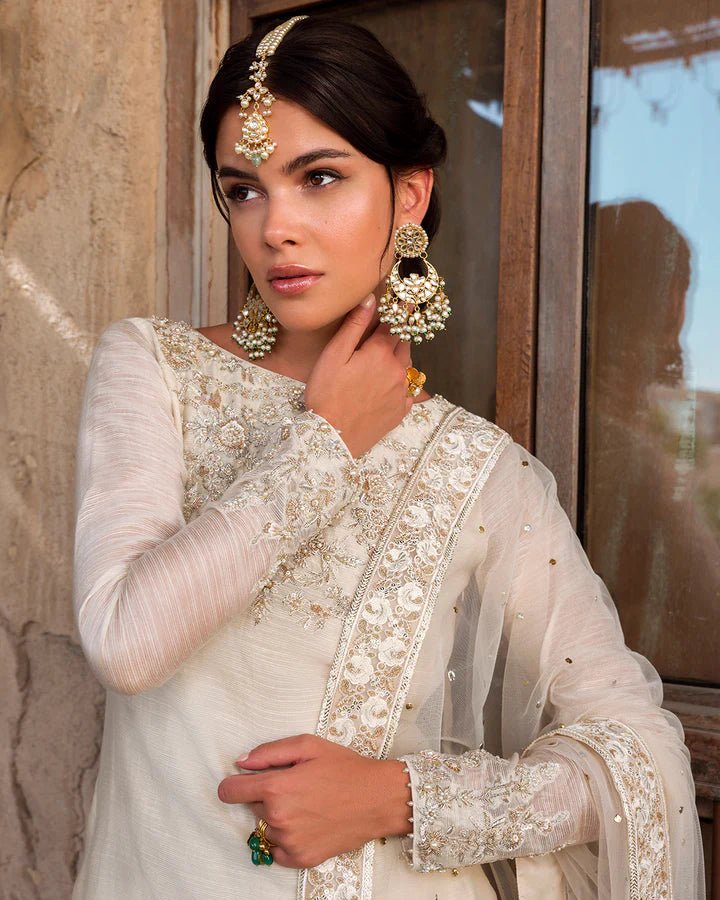 Model wearing an elegant ivory Raabi dress adorned with delicate embroidery from Faiza Saqlain's Luxe Formals Laira collection. Pakistani clothes online in UK.