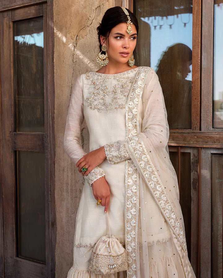 Model wearing an elegant ivory Raabi dress adorned with delicate embroidery from Faiza Saqlain's Luxe Formals Laira collection. Pakistani clothes online in UK.