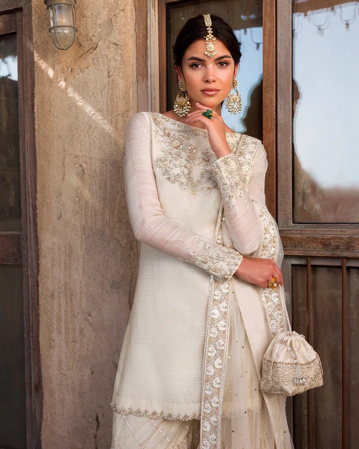 Model wearing an elegant ivory Raabi dress adorned with delicate embroidery from Faiza Saqlain's Luxe Formals Laira collection. Pakistani clothes online in UK.